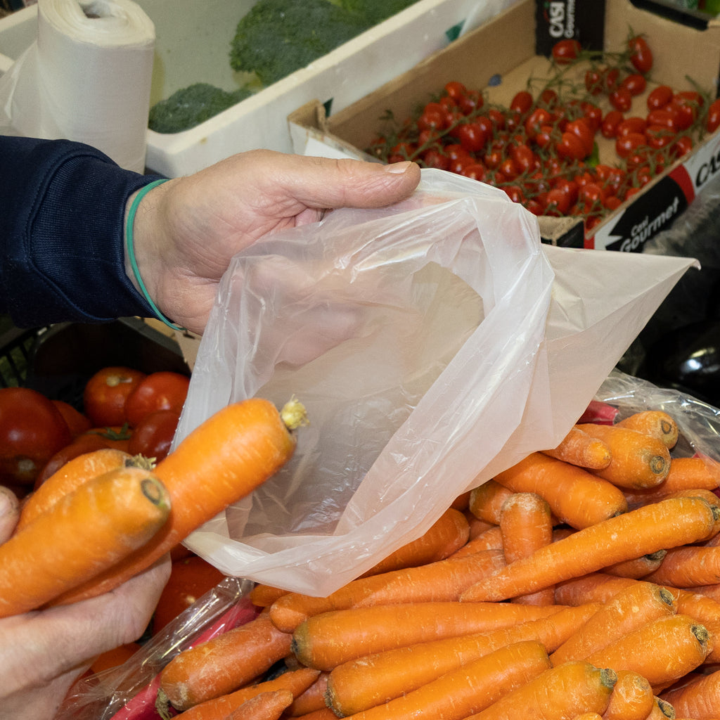 Persona llenando una bolsa de plástico transparente con zanahorias en la frutería